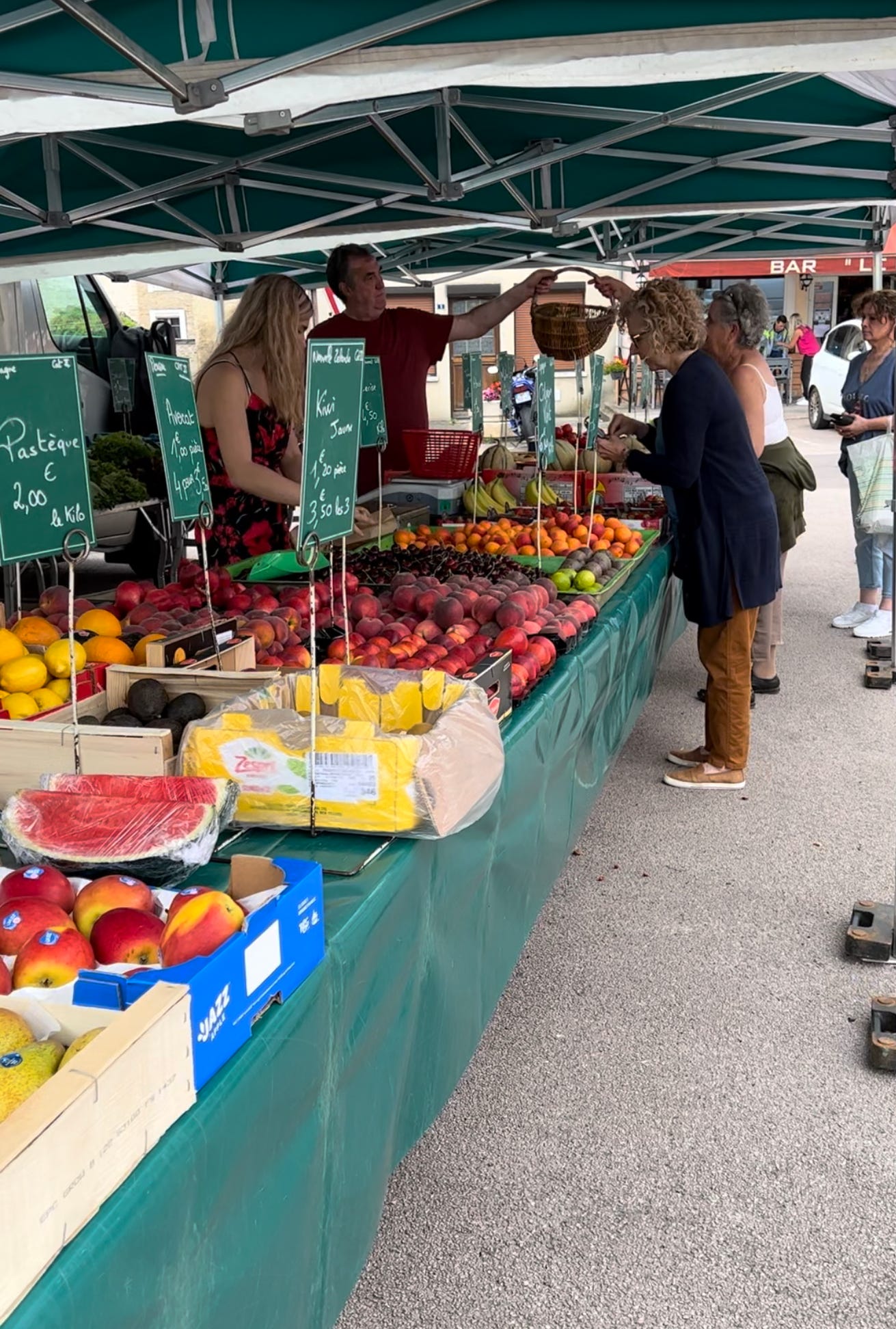 Photo of customers buying colorful summer fruit at a marketplace in Andelot, France