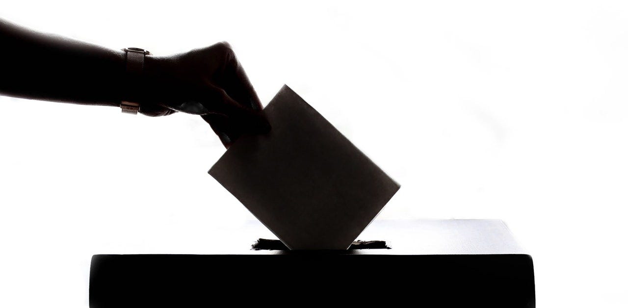 person’s hand dropping ballot into a voting box