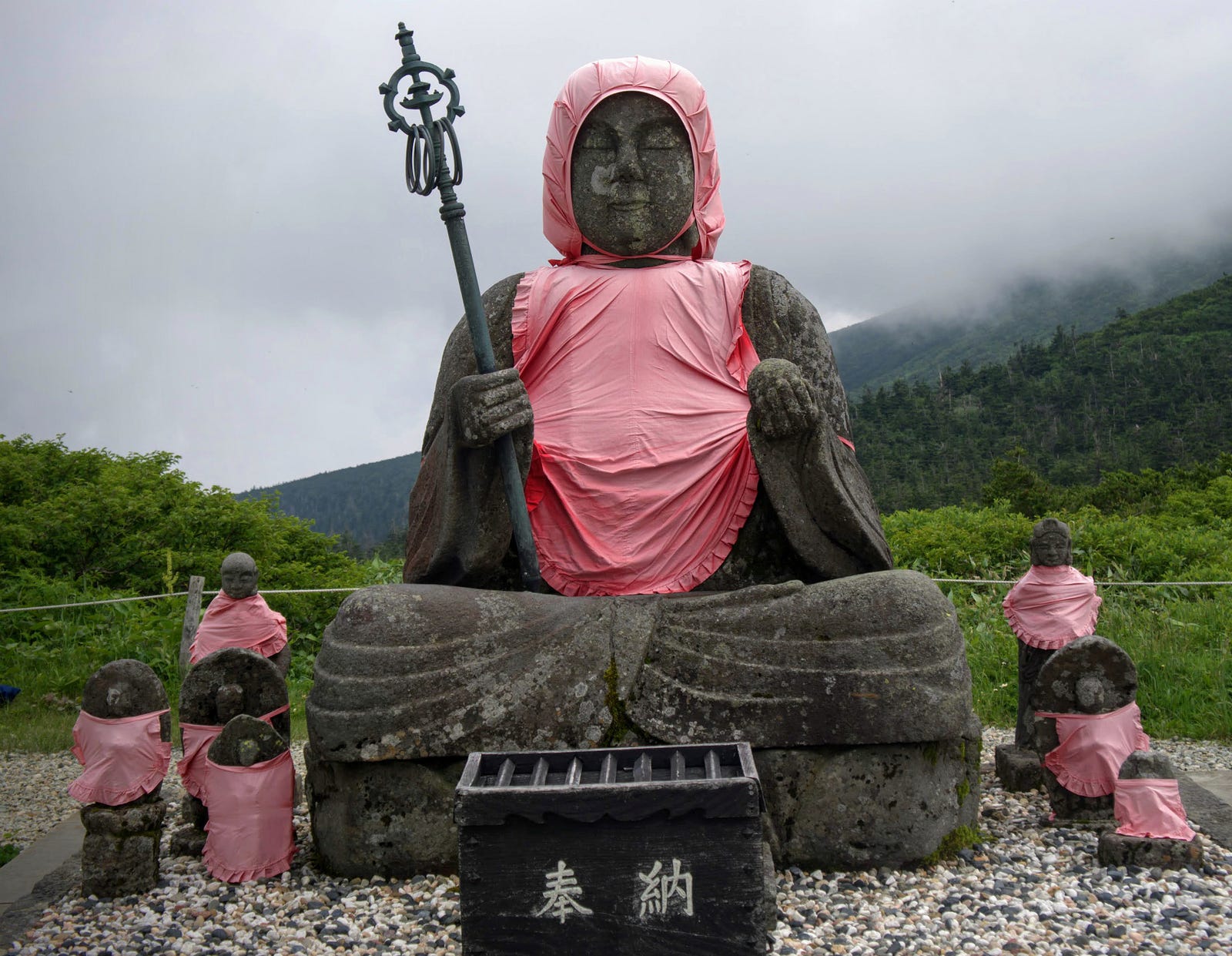 A close-up of the statues of Jizo on Jizo-dake wearing their characteristic red bibs, with a cloudy sky in the background.