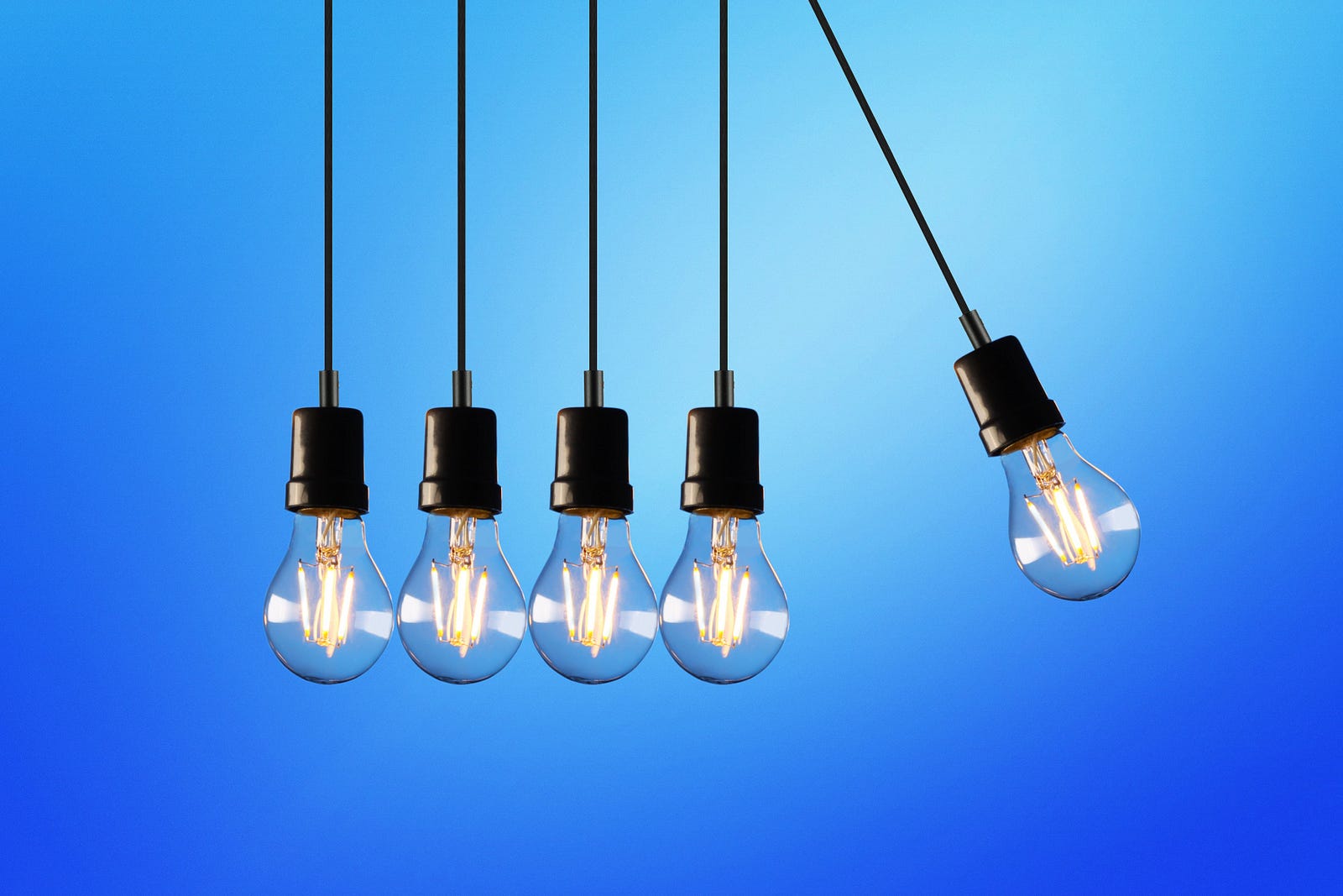 four light bulbs hanging in a row from cords, a fifth light bulb swings off at an angle