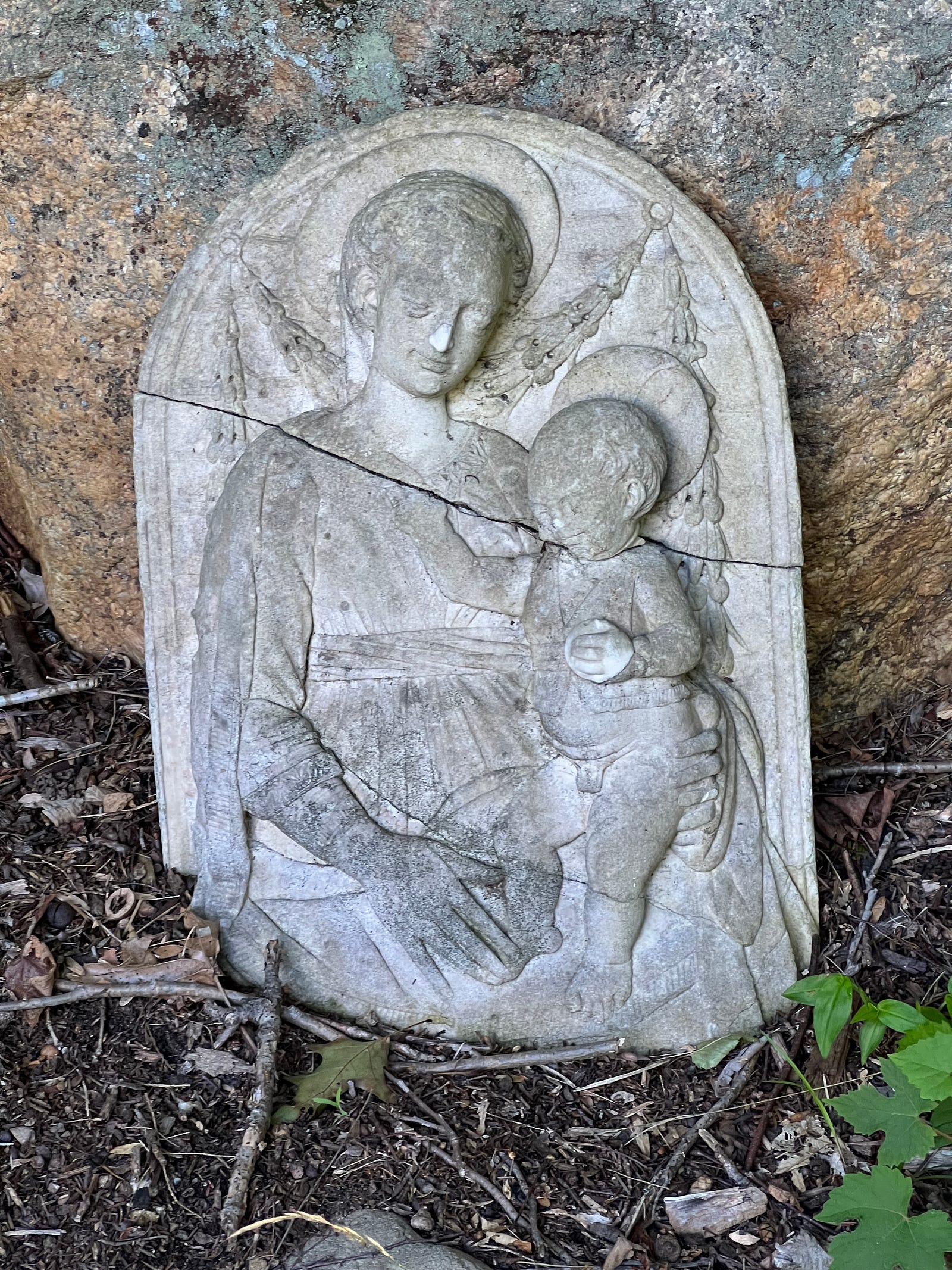 Photo of a stone madonna and child in an outdoor church garden. Both characters have the holy nimbus, or halo, behind their heads.