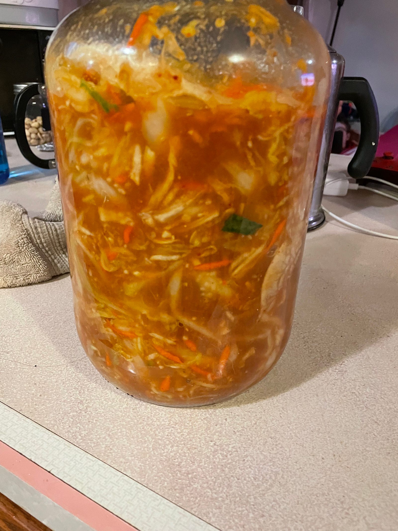 A gallon size pickle jar filled with kimchi sitting on the kitchen counter.