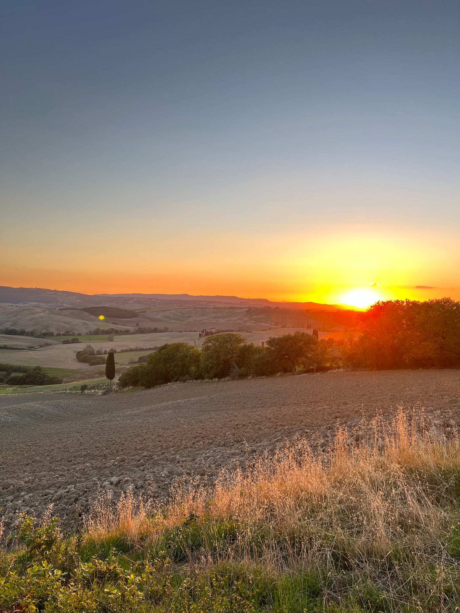 Photo of a stunning sunset overlooking plowed fields in the forground with the purpled badlands in the distance. Pienza, Tuscany.