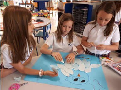 Tres niñas decoran un cartel en clase.