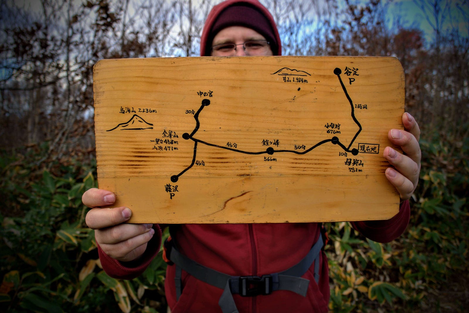 Hiker holds up a small wooden sign with a map of Mt. Hokari on the back