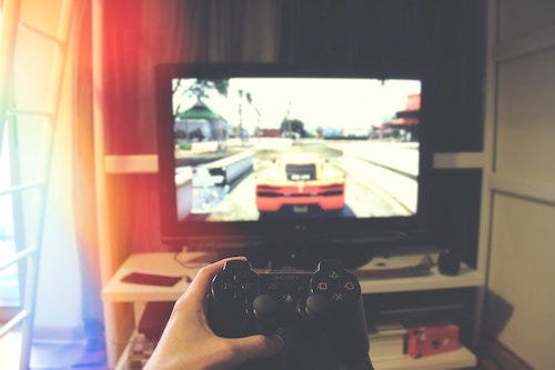 Someone holding a PS3 controller with one hand, and a blurry view of one of the Grand Theft Auto games on the TV in the background.