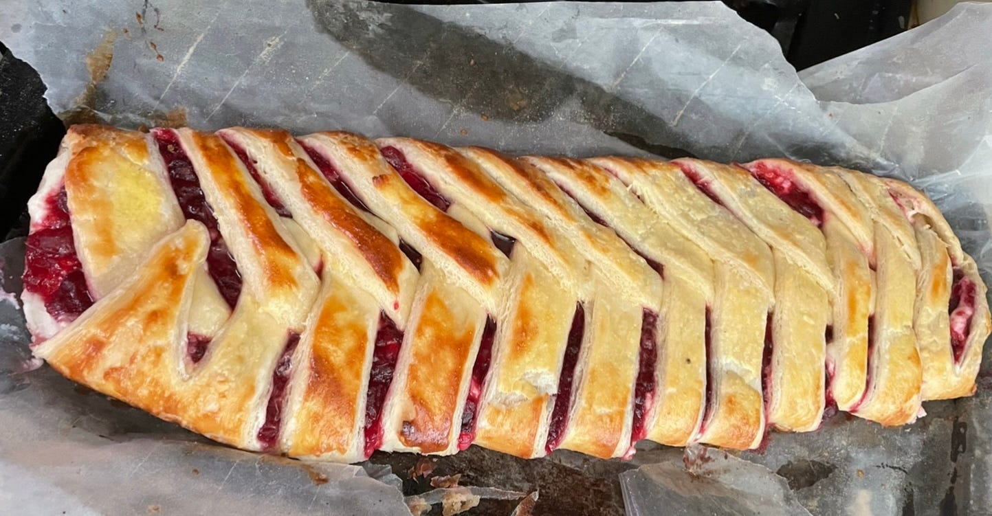 A close up of a braided crandberry cheese danish on wax paper just out of the oven.