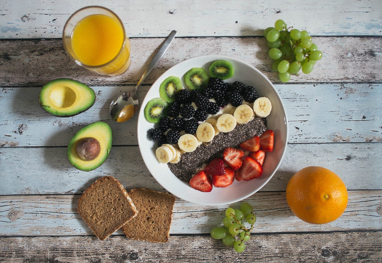 Una mesa con un frutero, jugo y otros alimentos saludables.