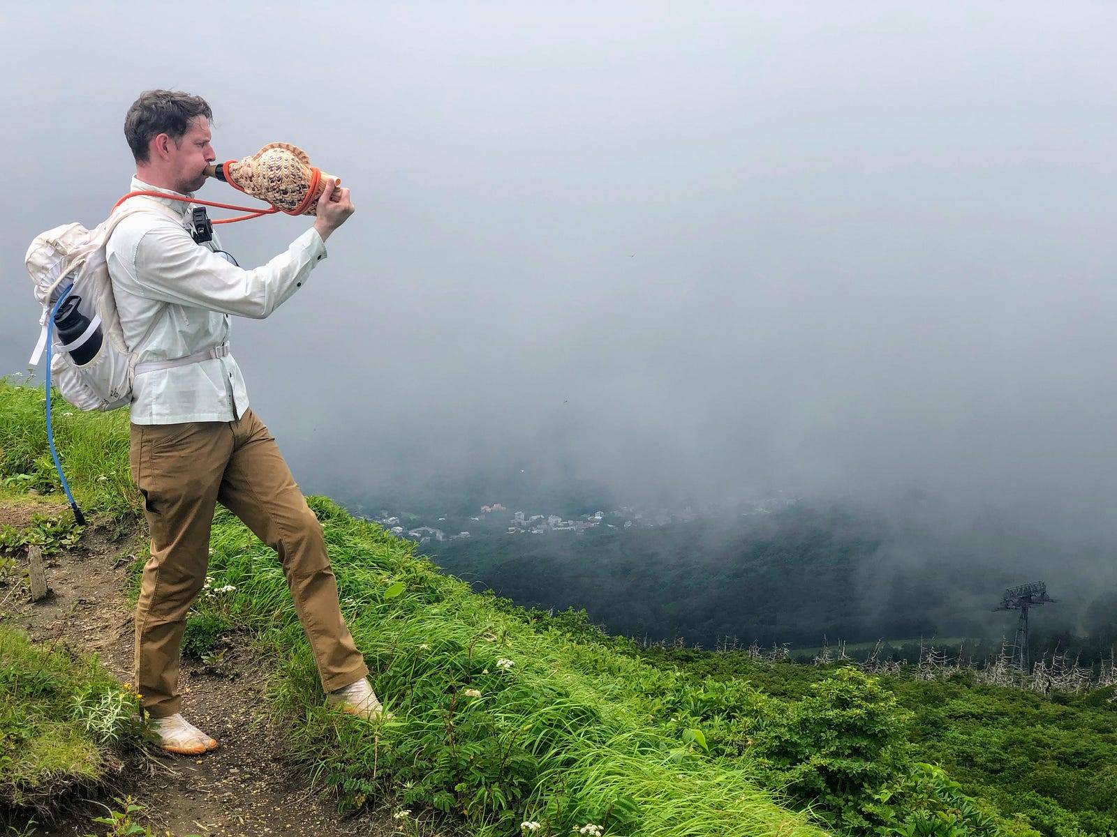 Tim Bunting AKA Kiwi Yamabushi blowing his conch at the summit of Jizo-dake, part of Zao-san, overlooking a Zao Onsen shrouded in cloud.