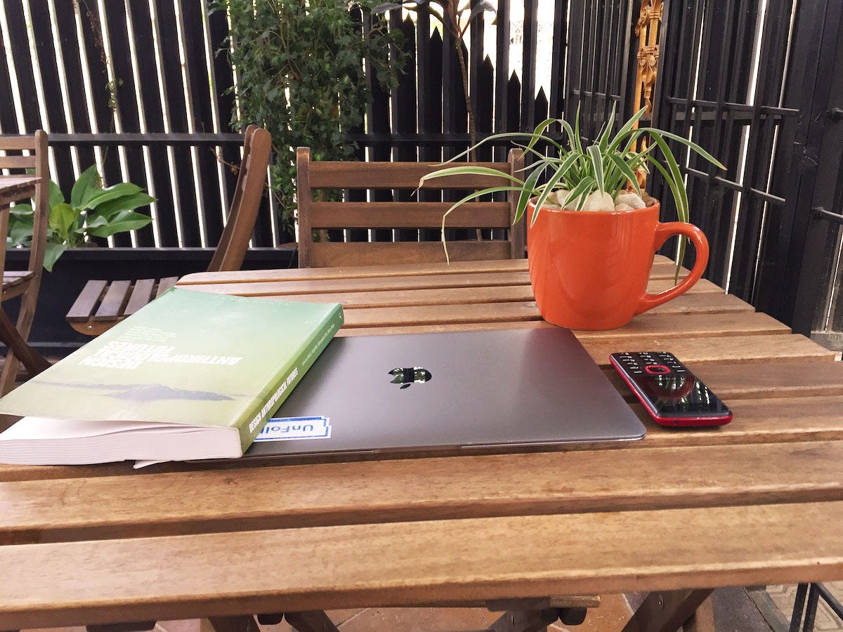 A book, MacBook and mobile phone on a table at a restaurant outdoors.