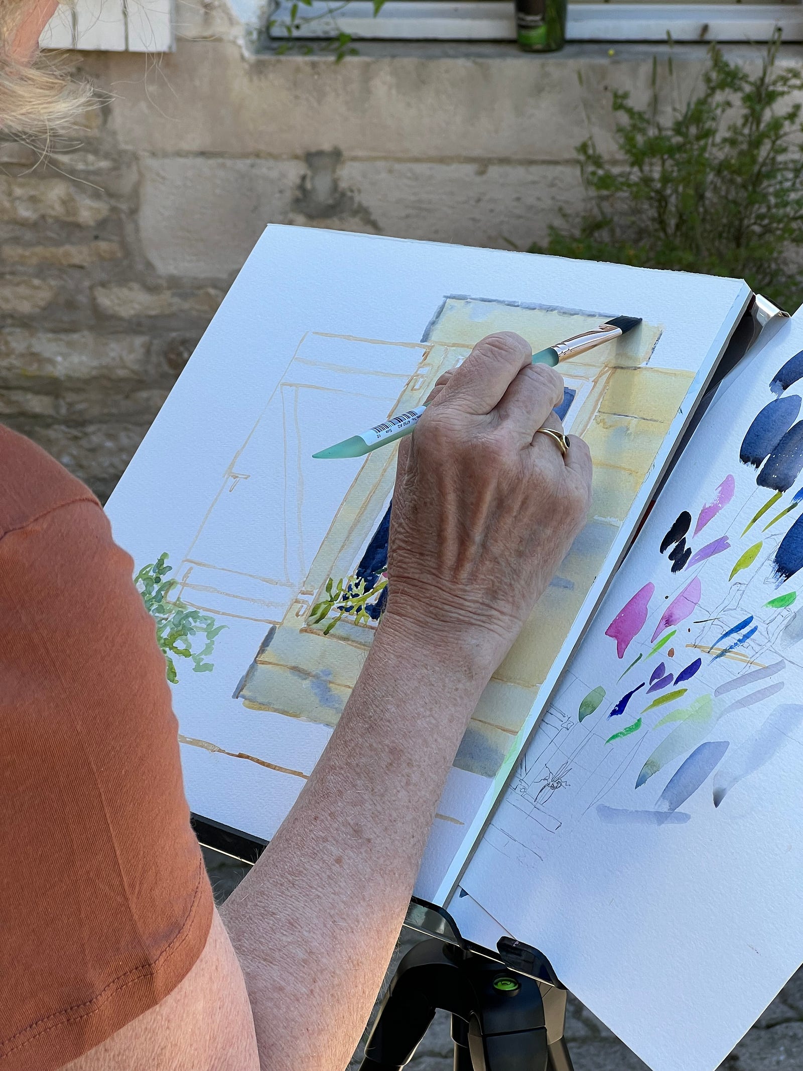 Photo of watercolor artist Roxanne Steed painting a jar of wildflowers at Chateau Orquevaux, France.