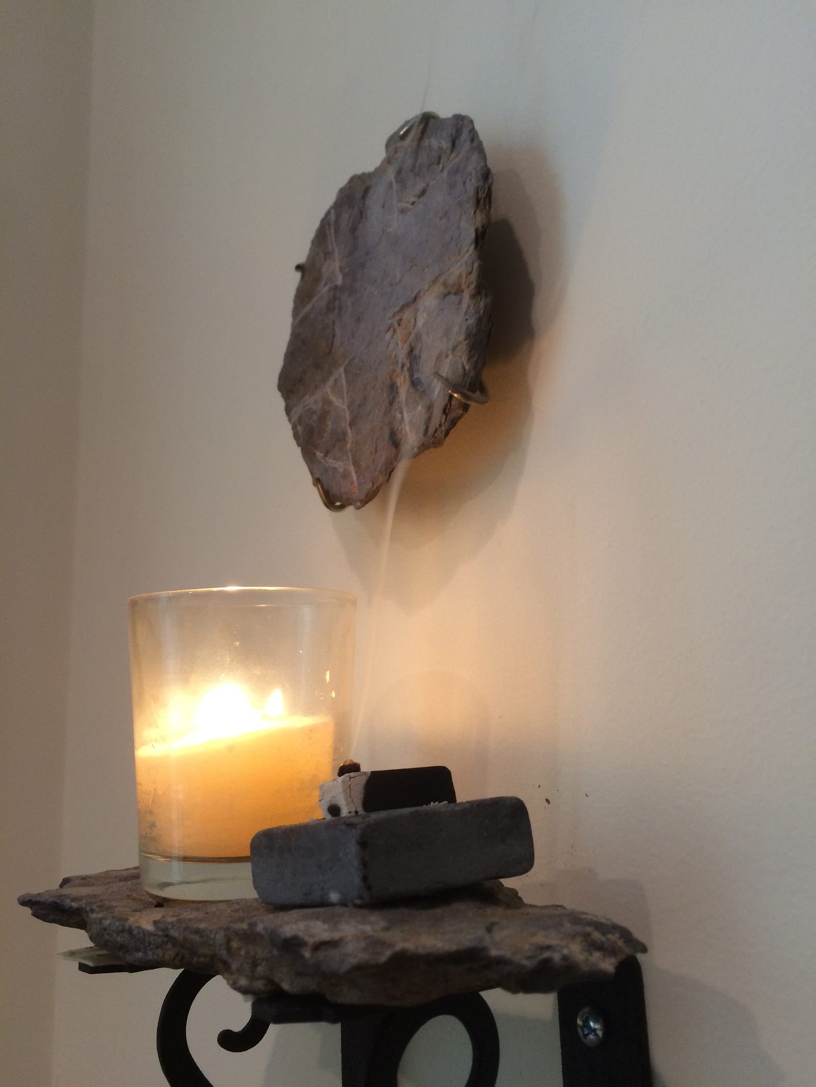 Photo of a candle and burning incense on a shelf below a cross fashioned from rock taken on Valentia Is, Ireland.