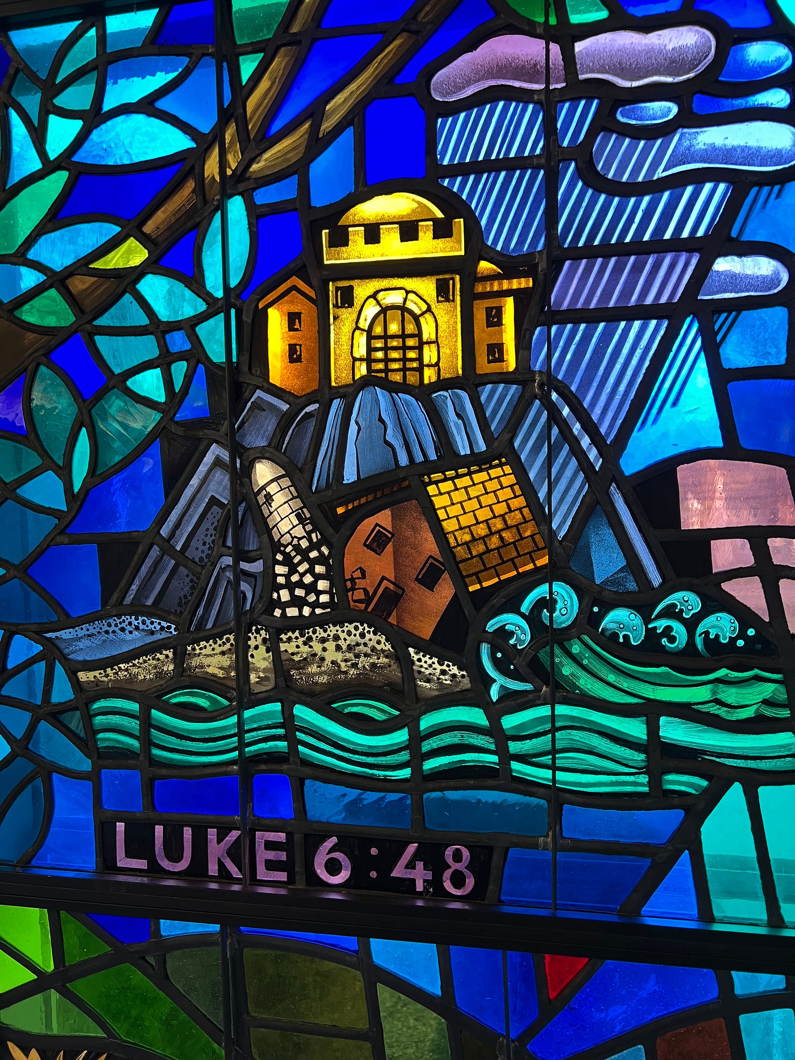Photo of a portion of stained glass at St Andrew’s Madison, CT showing the stormy waters wreaking the house built on sand in Luke 6.