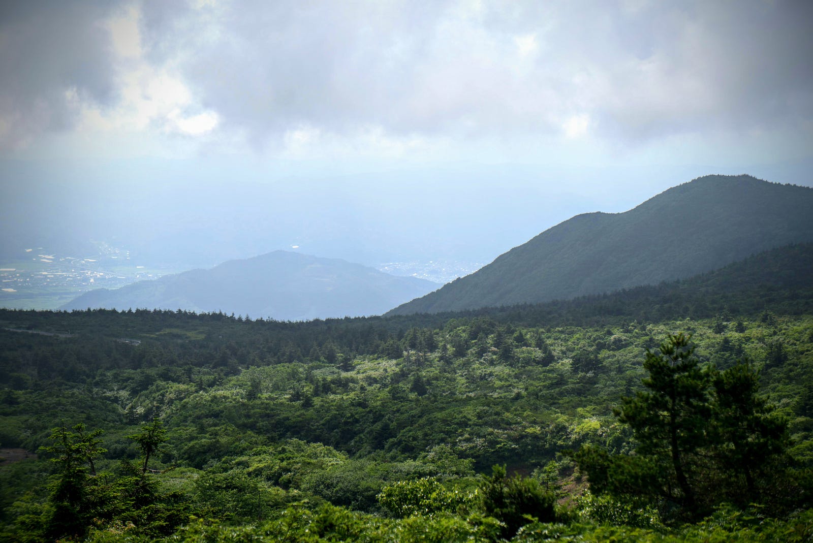 Looking towards Yamagata City from the Katta Lift of Zao-san (Mt. Zao) over the green forests and mountains, city in the distance under a cloudy sky.