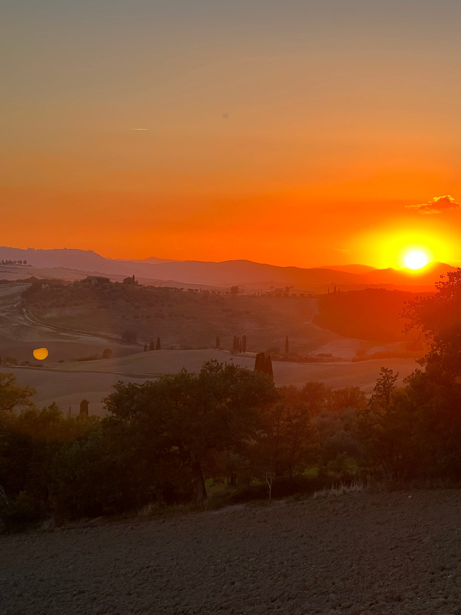 Photo of a sunset in Pienza Tuscany, as the sun touches the distant hills, and blankets the fields with warm golden light…