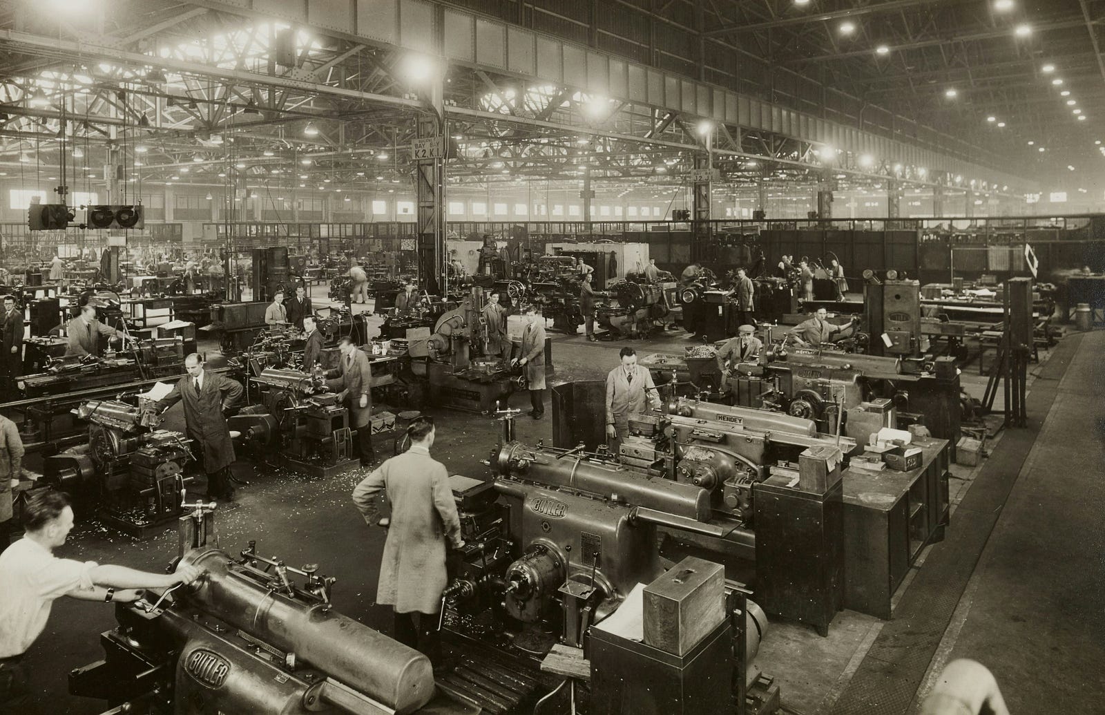 Workers assembling engines in a World War II factory, illustrating industrial production and innovation under capitalism.