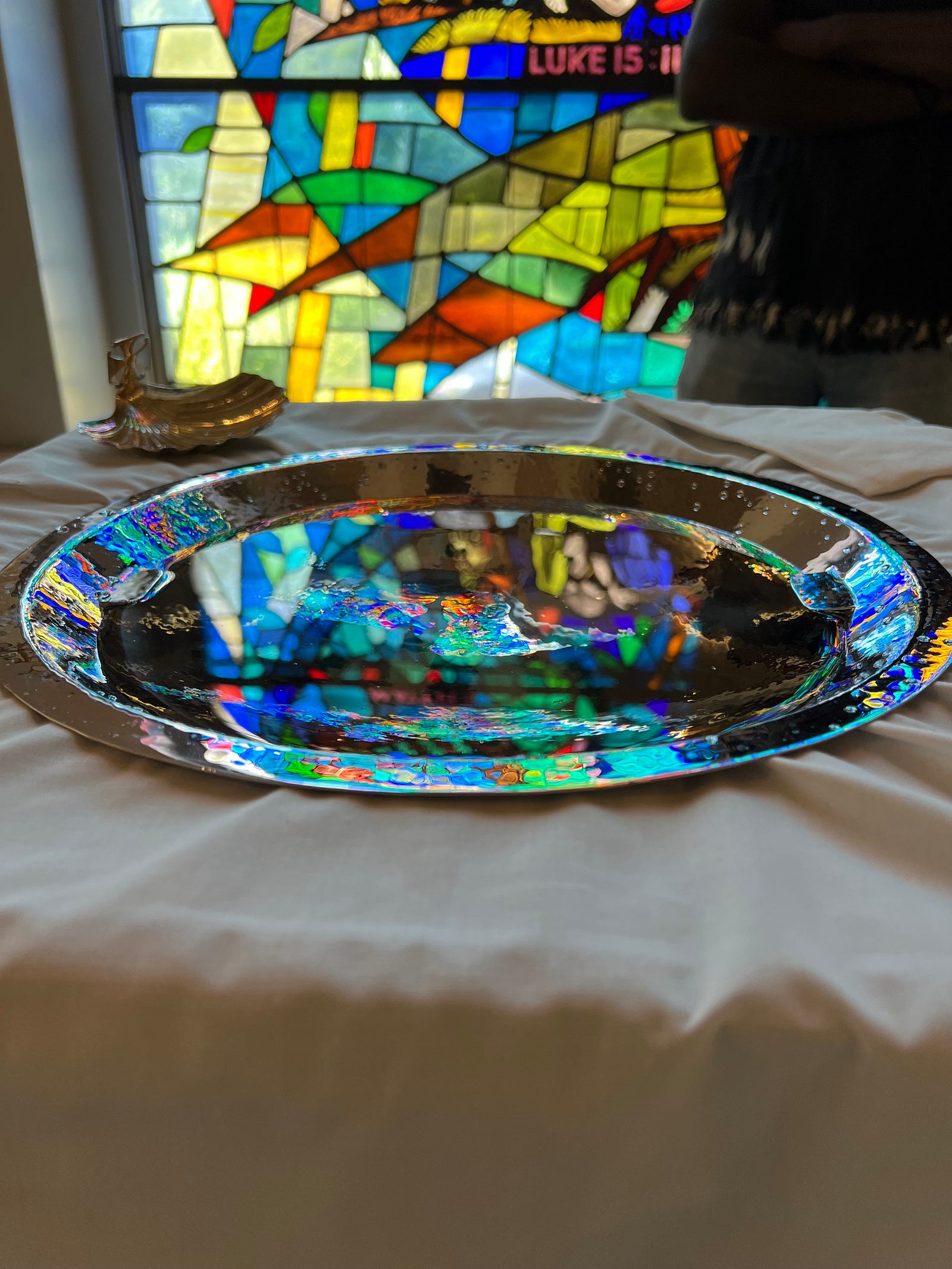 Photo of the baptismal font at St Andrews, awash in a riot of color from the stained glass behind.