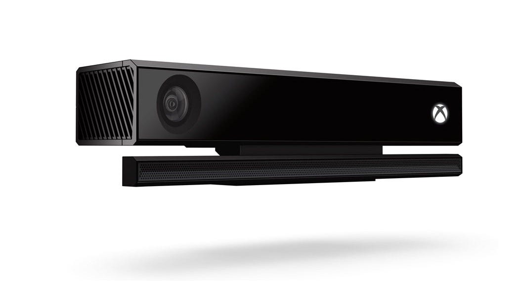 A promotional image of a long, narrow, rectangular camera device floating above the ground. The Xbox logo, an X within a glowing white circle, is displayed on the device’s far right side.