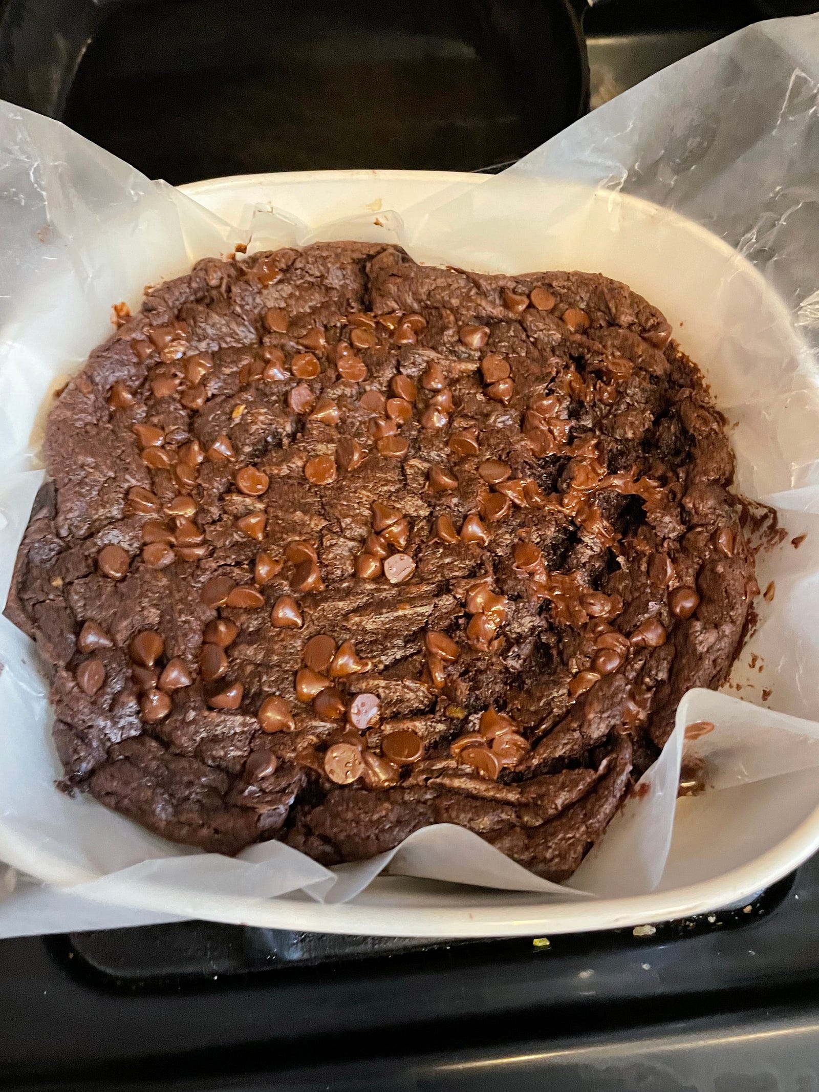Brownies fresh out of the oven with goowy melting chocolate chips on top, surrounded by wax paper still in the pan.