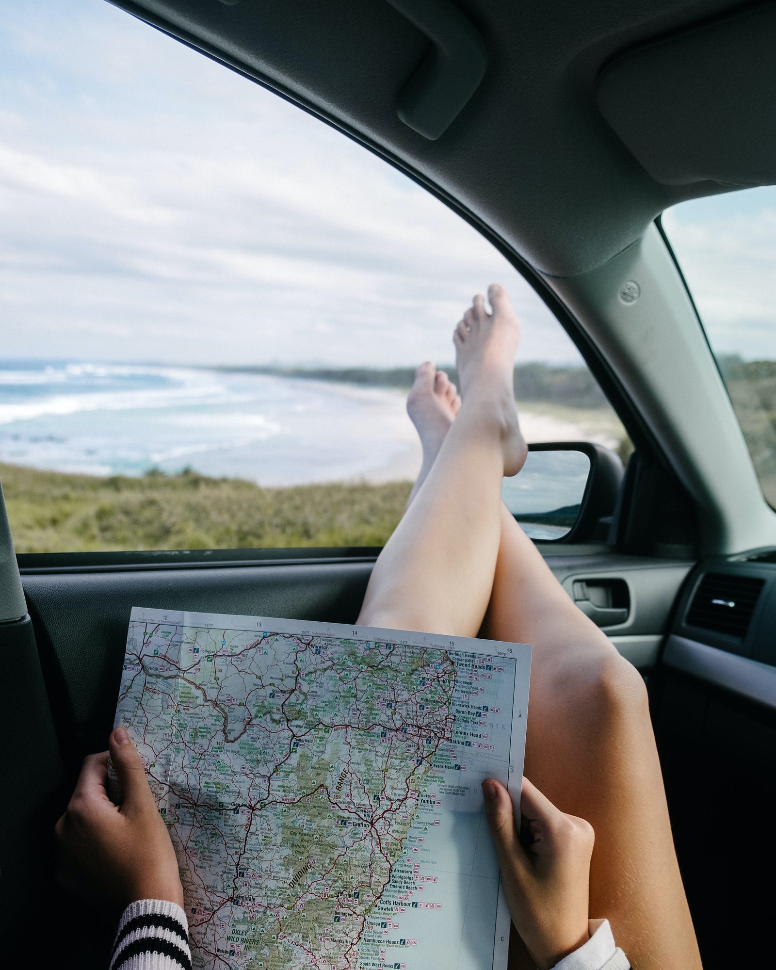 A girl holding a map, ridding in a car with her feet hanging out the window