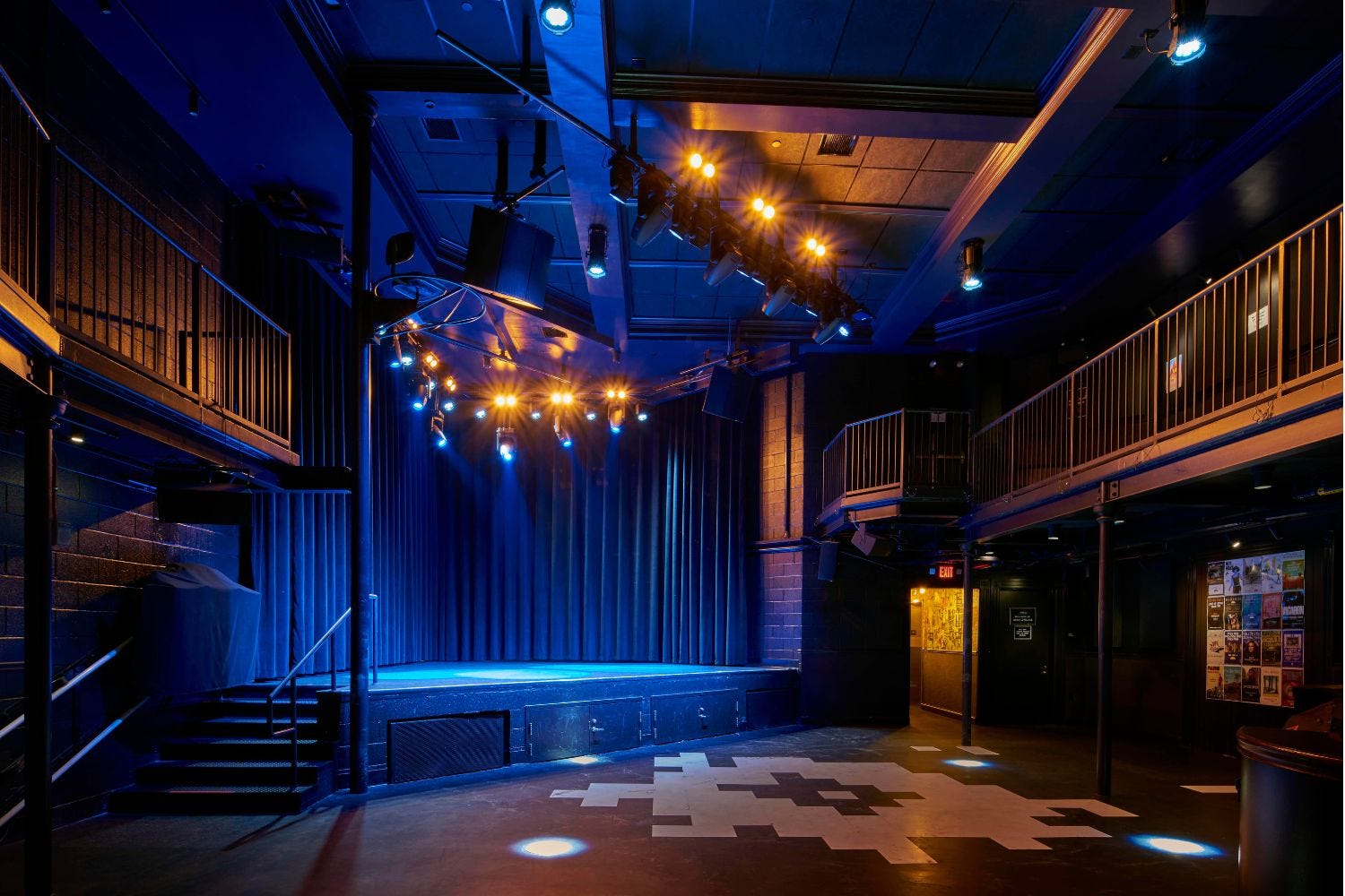 The empty interior of The Atlantis, with the small stage in the front corner and the house lights on over two tiers of floors for the audience to stand.
