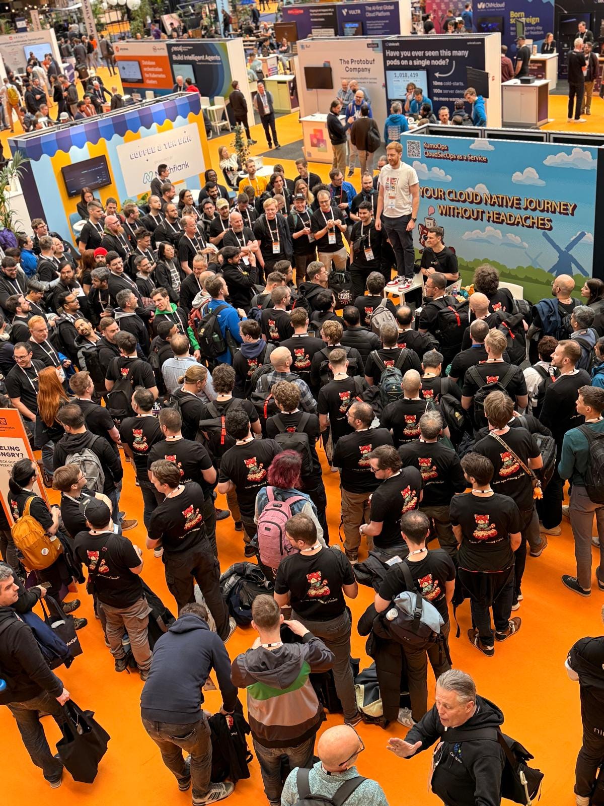 (The KumoOps booth): A large crowd of people standing in front of a colorful booth at KubeCon EU 2026.