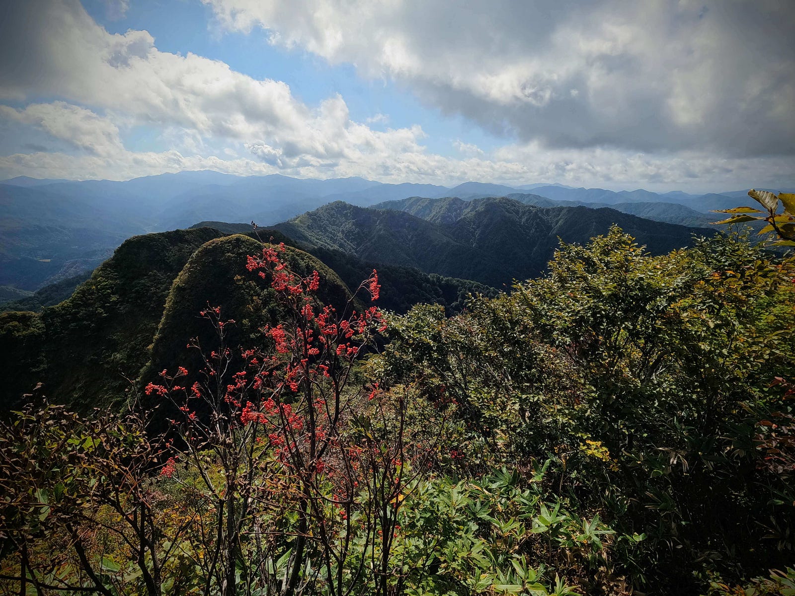 View over the surrounding mountains getting ready to change for the autumn, with a bright blue sky covered in ominous clouds at the summit of Mt. Maya, one of the 100 Famous Mountains of Yamagata