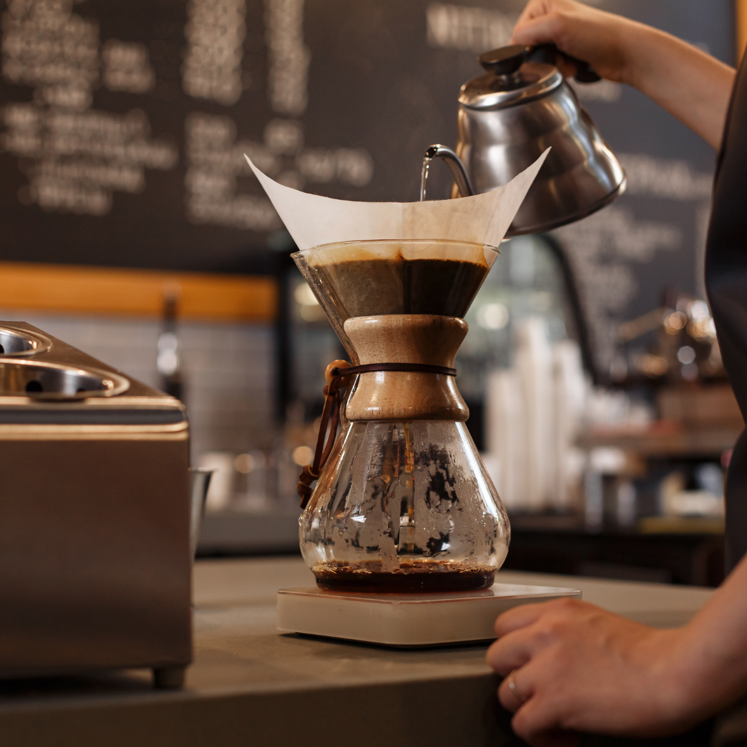 A barista pour hot water into a Chemex coffee brewer to make fresh, great-tasting coffee.