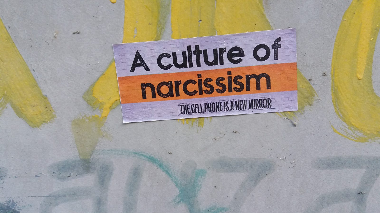 Sticker on a wall reading ‘Culture of Narcissism,’ symbolizing society’s obsession with self-image and social media validation.