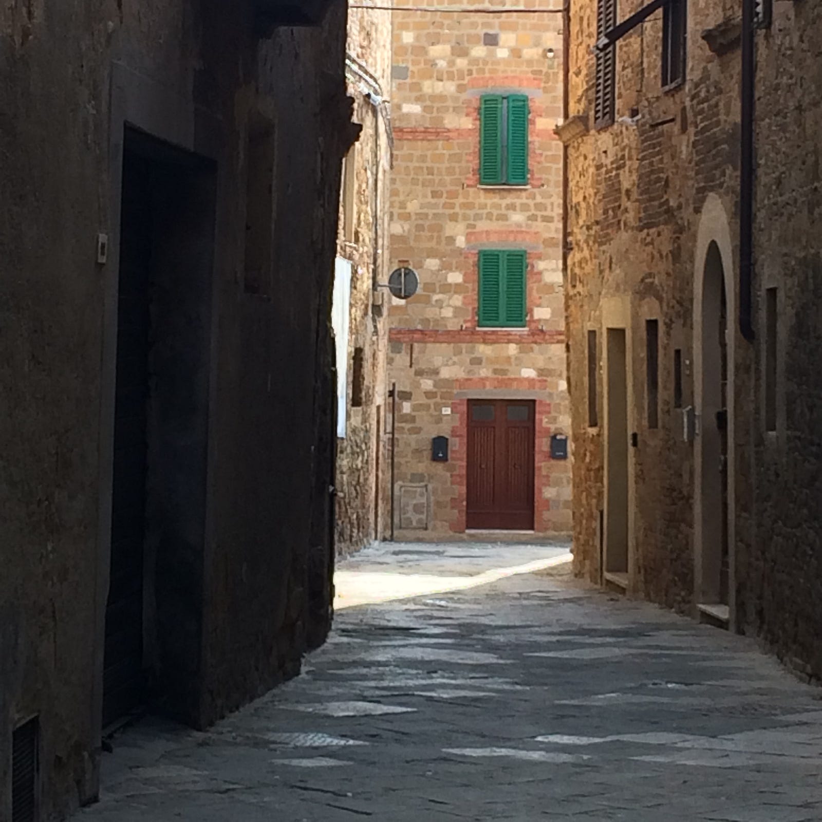 Photo of a shaded, cobbled street in Pienza, Tuscany, that turns a corner into a sunlit way.
