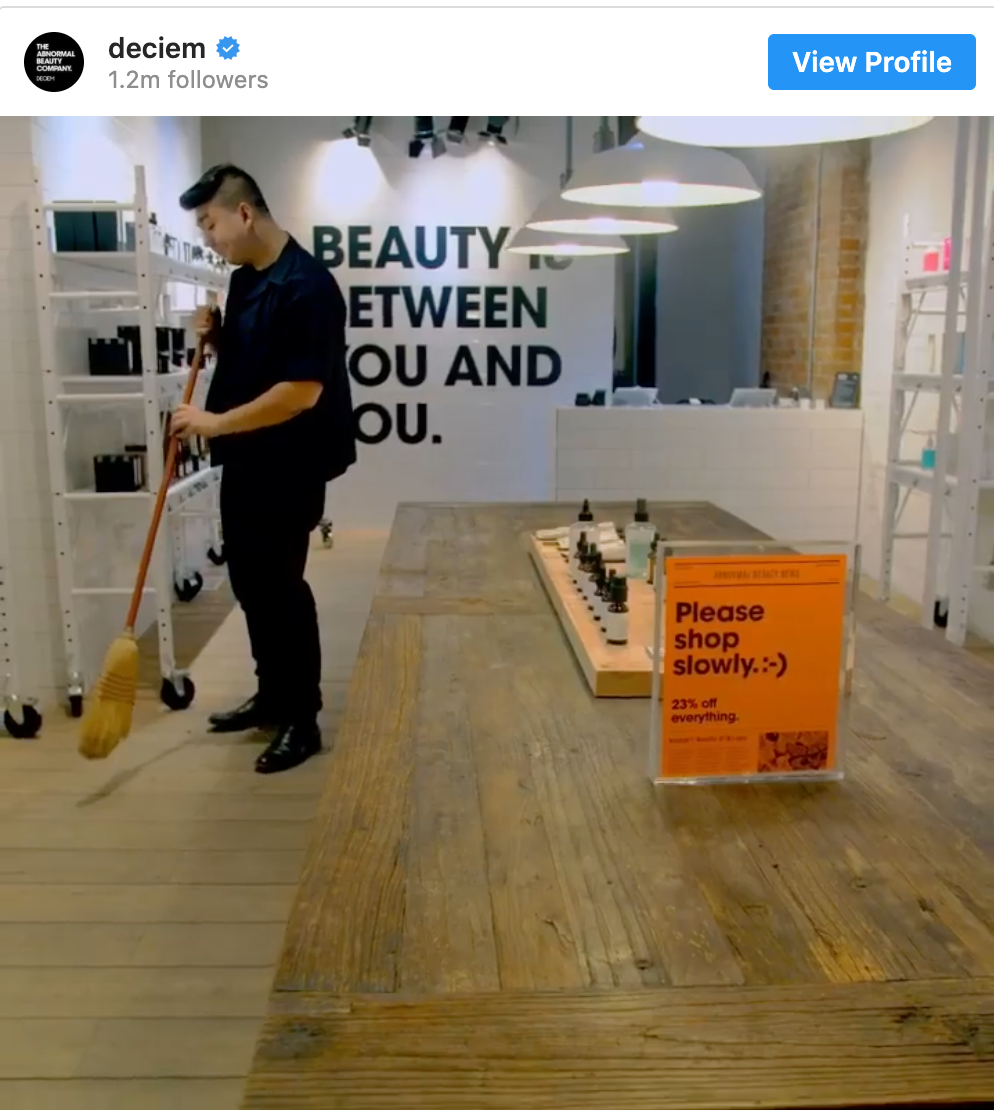 Inside Deciem, an employee sweeps the floor, and an orange sign that says “Please shop slowly; 23% off everything”