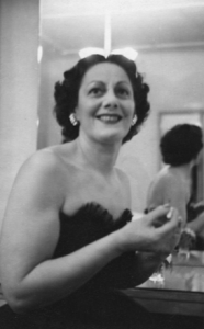 Mother sits in front of dressing room mirror with makeup, black and white photograph