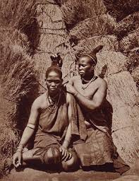 a picture of two african women in front of a hut during the precolonial times