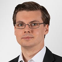 Portrait Dr. Steven Arzt, a man with glasses and glossy hair and a clean shaven face, wearing a white shirt with a black sakko on top.