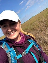 a woman smiles while standing in an open field