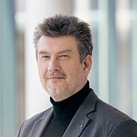 Portrait of Prof. Dr. Martin Steinebach, a man with salt&pepper hair, a beard shadow and a black turtleneck
