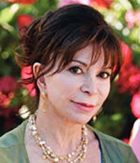 Isabel Allende glancing at the camera. She is wearing a light green shirt and gold jewelry.