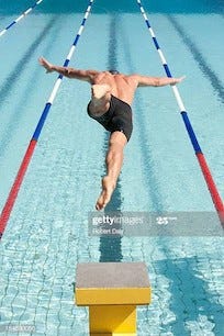 Swimmer leaping off starting block into the pool. He has a clear lane in which to swim.