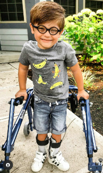 A child with cerebral palsy is smiling while standing up holding onto his walker.