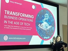 Presentation on large screen that states “Transforming Business Operations in the Age of Tech” and the author is standing in front of the presentation holding up the peace sign.