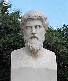 A stone bust of a man with a curly beard against a blue sky