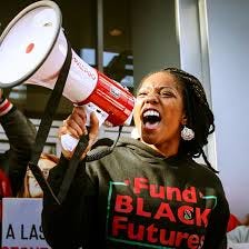 Black woman in a hoodie with braided hair speaking into a megaphone