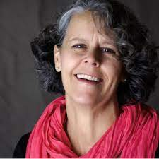 Kim Ducharme — a woman with short black curly hair with in red scarf smiling.