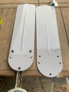 Two white fan blades lying side by side with 3 holes drilled into each one. 