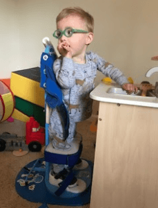 A child standing up independently with the help of an adapative standing device.