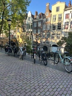 A photograph of some bicycles parked alongside a canal in Utrecht, with a row of buildings in typical Dutch architecture shown in the background.