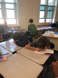 Three students around the classroom writing in their notebooks.