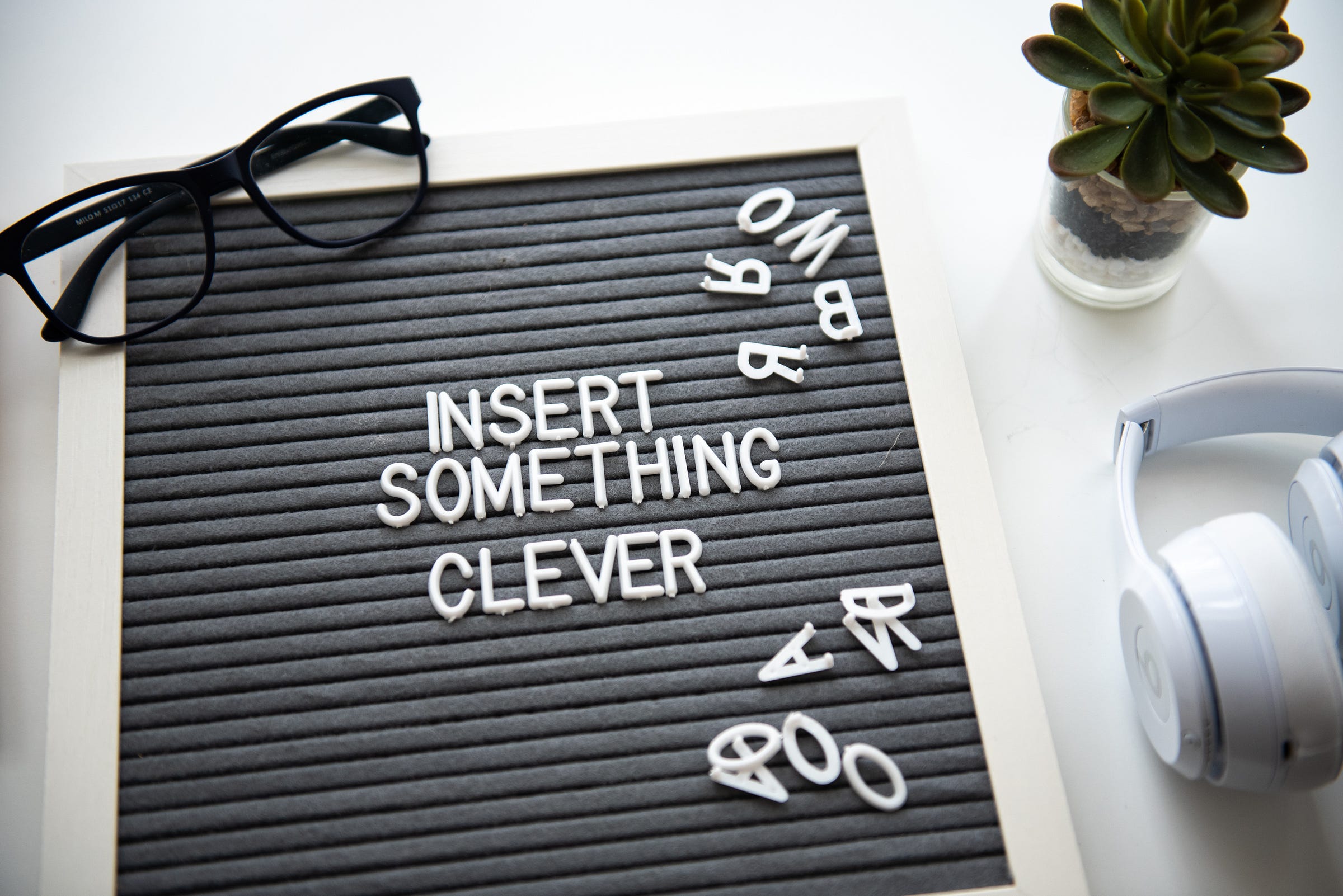 a black notice board with the words ‘insert something clever’ and a pair of black glasses and a plant