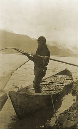 a historical sepia colored photo of a man with a net standing in a canoe full of small fish