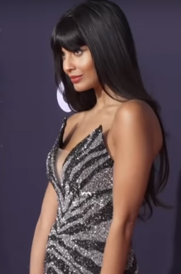 Jameela standing in profile against purple background, wearing sleeveless black and silver sparkly gown